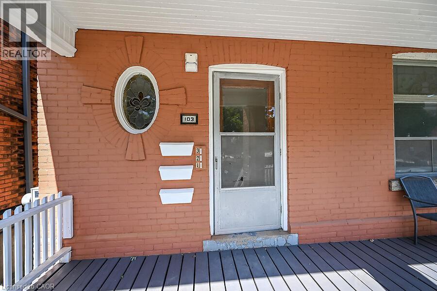 Brick facade with an oval stained-glass window, a screened entry door, and a porch featuring composite decking and a white railing - 103 Mary Street, Hamilton, ON - Outdoor With Deck Patio Veranda With Exterior