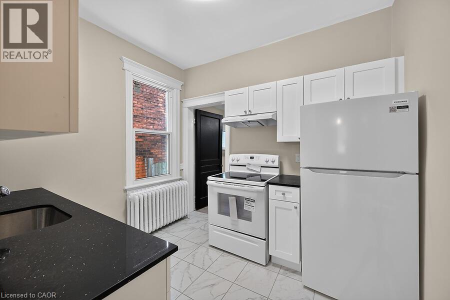 Kitchen featuring white shaker-style cabinetry, black speckled countertops, a double-basin stainless steel sink, and white appliances - 103 Mary Street, Hamilton, ON - Indoor Photo Showing Kitchen