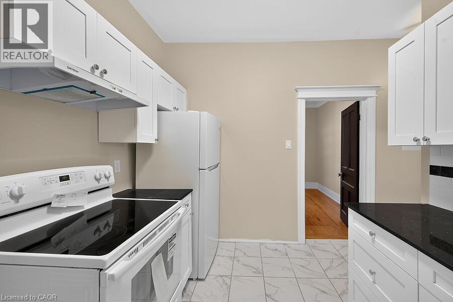 Kitchen featuring white shaker cabinetry, dark countertops, a white electric range, and a white refrigerator - 103 Mary Street, Hamilton, ON - Indoor