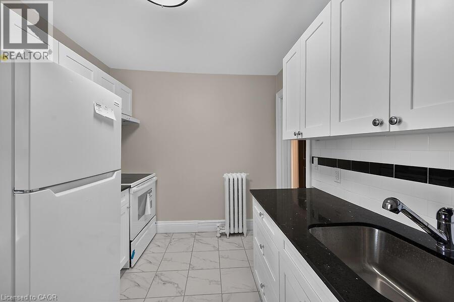 Galley kitchen featuring white cabinetry, dark speckled countertops, and a subway tile backsplash with a black accent band - 103 Mary Street, Hamilton, ON - Indoor