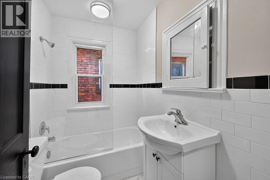 White subway tile bathroom featuring a single window, built-in bathtub with shower, pedestal sink, and medicine cabinet - 103 Mary Street, Hamilton, ON - Indoor Photo Showing Bathroom