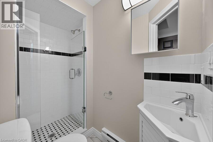 Walk-in shower featuring a glass enclosure, subway tile surround with a black accent band, and a mosaic tile floor - 103 Mary Street, Hamilton, ON - Indoor Photo Showing Bathroom