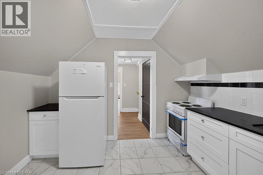 Kitchen featuring white cabinetry, dark countertops, white subway tile backsplash with a black accent, and marble-look floor tile - 103 Mary Street, Hamilton, ON - Indoor Photo Showing Kitchen