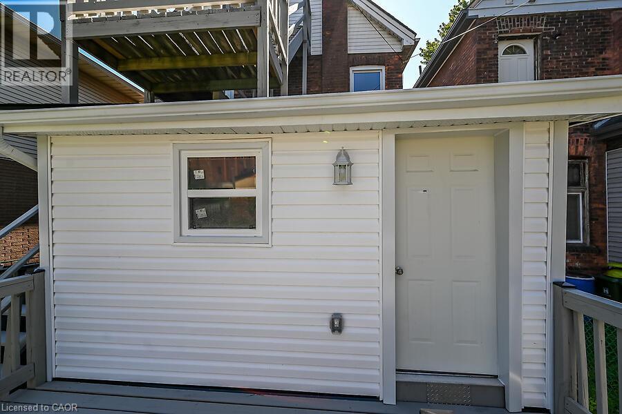 Exterior featuring white horizontal siding, a paneled door, and a window with white trim - 103 Mary Street, Hamilton, ON - Outdoor With Exterior