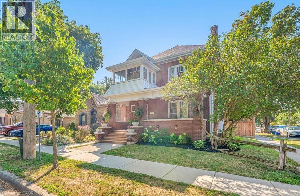 Brick facade residence featuring a covered porch with column supports, an enclosed upper-level balcony, a prominent chimney, a pitched roof, and established front yard landscaping - 47 Eagle Avenue, Brantford, ON - Outdoor