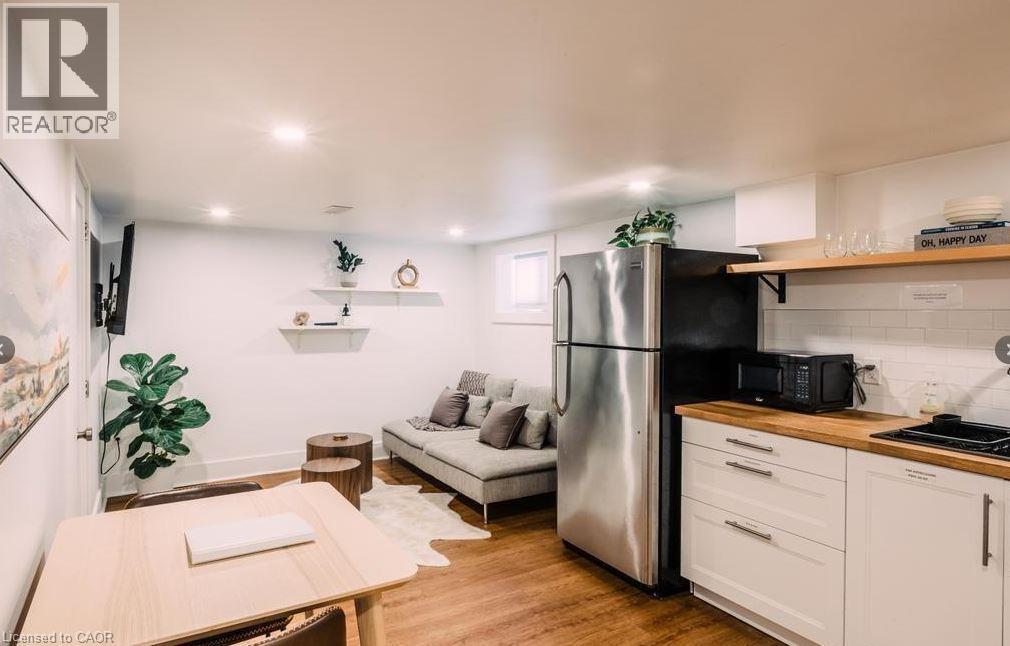 Compact kitchen area featuring a stainless steel refrigerator, wood-finish countertops, white cabinetry with contemporary hardware, and a white subway tile backsplash - 47 Eagle Avenue, Brantford, ON - Indoor Photo Showing Kitchen