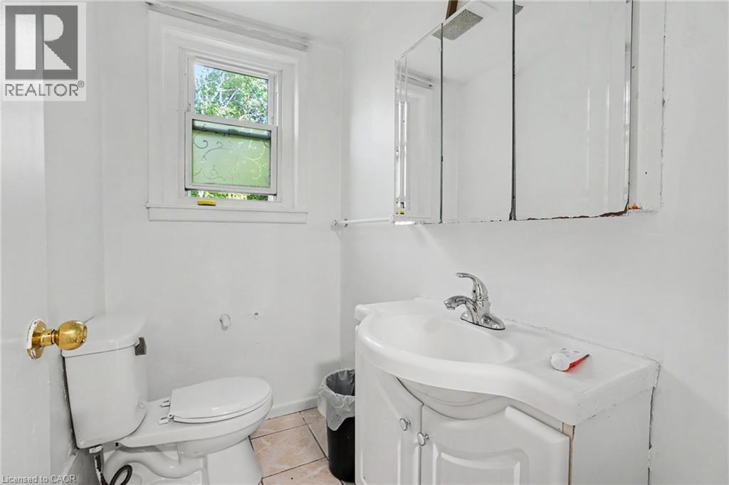 Bathroom featuring a window with patterned glass, white ceramic toilet, white vanity with integrated sink, chrome faucet, and mirrored medicine cabinet - 47 Bowman Street, Hamilton, ON - Indoor Photo Showing Bathroom