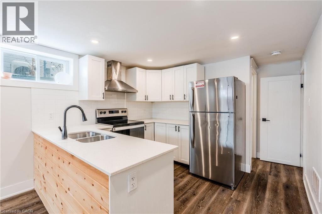 Modern kitchen featuring white shaker cabinetry, stainless steel appliances, a wood-paneled island with an undermount double sink, white countertops, and wood-finish flooring - 16 Ronaldshay Avenue, Hamilton, ON - Indoor Photo Showing Kitchen With Double Sink