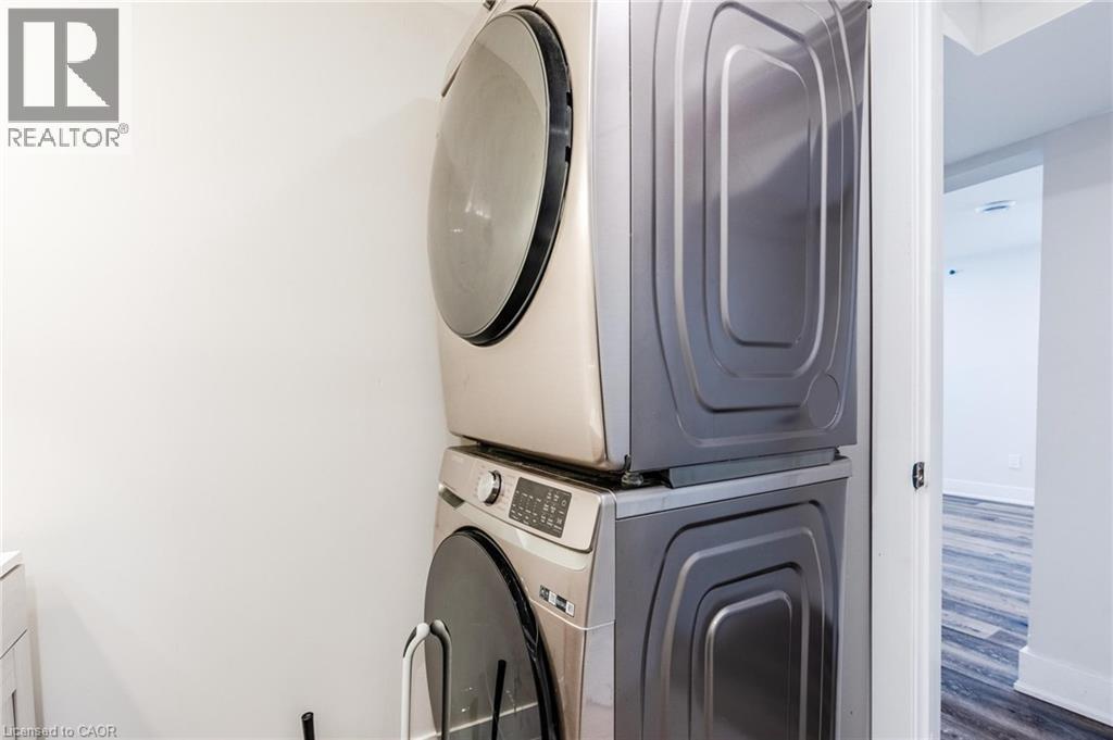 Laundry area featuring a stackable washer and dryer, white walls, and wood-finish flooring visible through the doorway - 16 Ronaldshay Avenue, Hamilton, ON - Indoor Photo Showing Laundry Room
