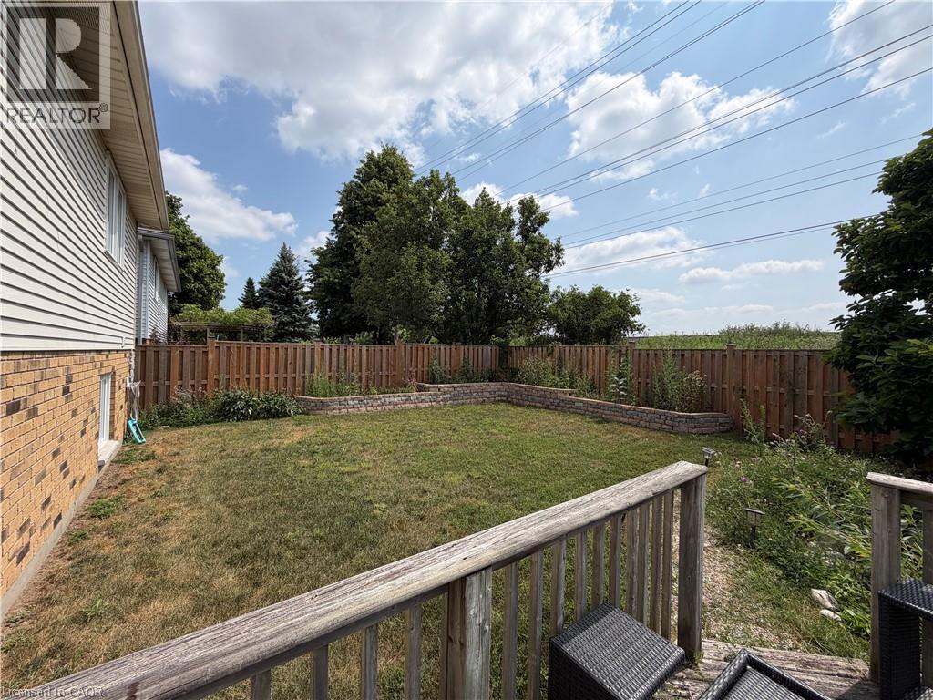 Fenced backyard featuring a wood deck, manicured lawn area, and stone retaining walls - 436 Gatestone Boulevard, Waterloo, ON - Outdoor