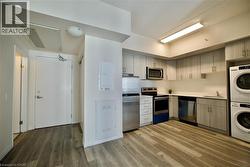 Contemporary kitchen featuring wood-finish flooring, light-toned cabinetry, stainless steel appliances, and stacked laundry machines -