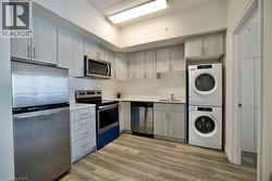 Kitchen featuring stainless steel appliances, wood-finish flooring, light-toned cabinetry, solid surface countertops, and stacked laundry appliances -