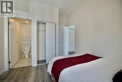 Bedroom featuring wood-finish flooring, a sliding closet door, and a private three-piece bathroom with a toilet, tile flooring, and integrated shelving -