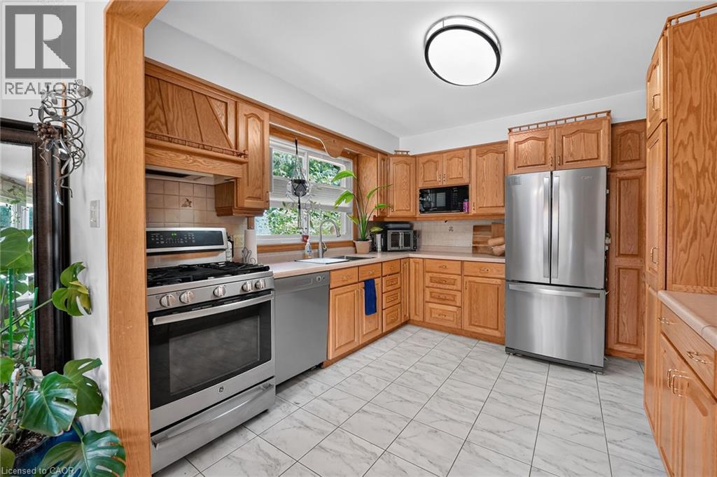 Kitchen featuring natural wood cabinetry, stainless steel appliances, light-toned countertops, tile flooring, and a window with outdoor views - 3 Orchard Parkway, Grimsby, ON - Indoor Photo Showing Kitchen With Double Sink