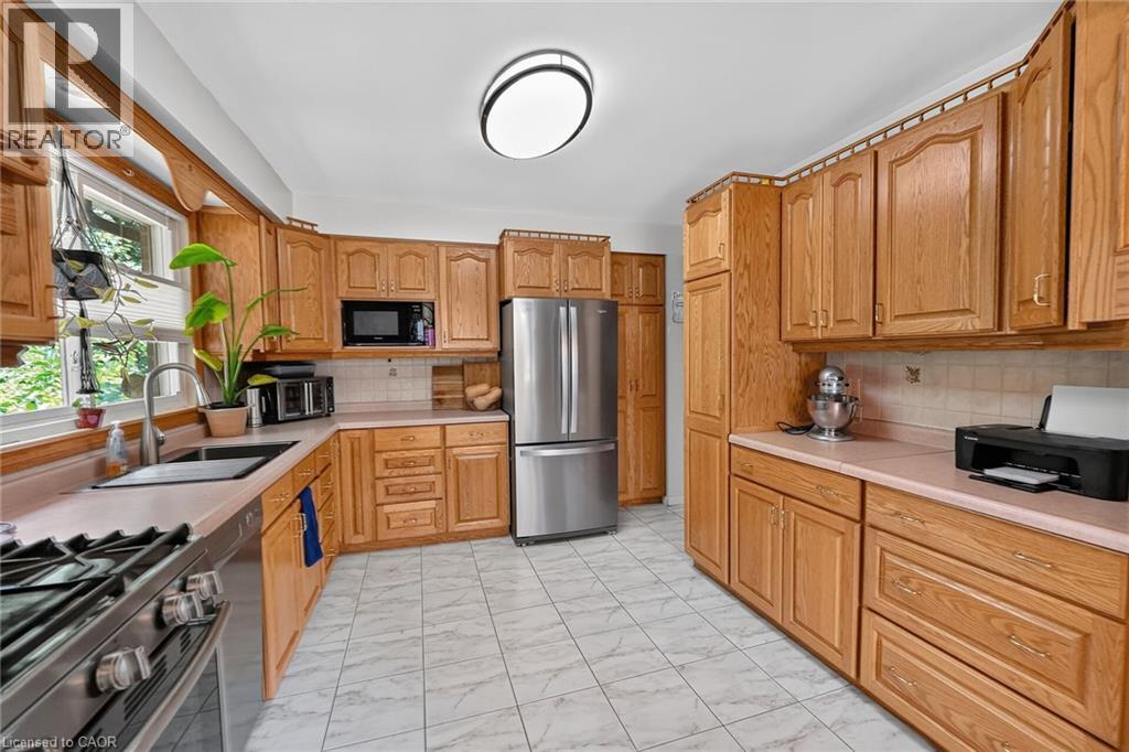 Kitchen featuring extensive wood cabinetry, L-shaped countertop space, stainless steel appliances, and tile flooring - 3 Orchard Parkway, Grimsby, ON - Indoor Photo Showing Kitchen