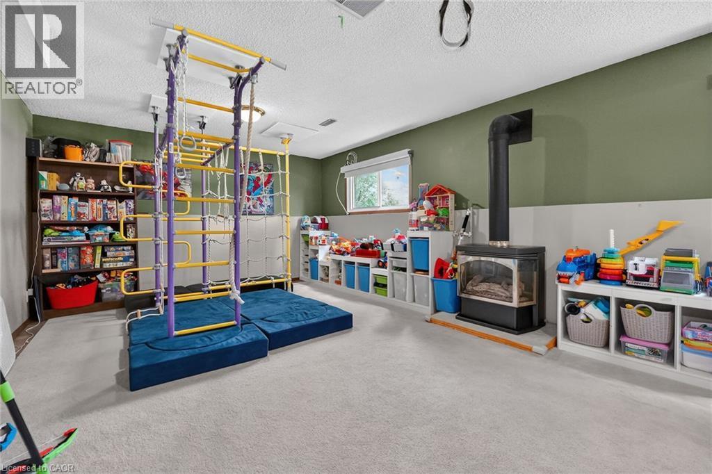 Carpeted basement room featuring a freestanding stove, a window, and recessed lighting - 3 Orchard Parkway, Grimsby, ON - Indoor