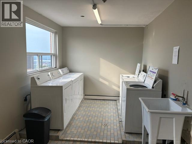 Dedicated laundry room featuring multiple washing machines, dryers, a utility sink, and a large window - 30 Summit Avenue Unit# 604, Hamilton, ON - Indoor Photo Showing Laundry Room