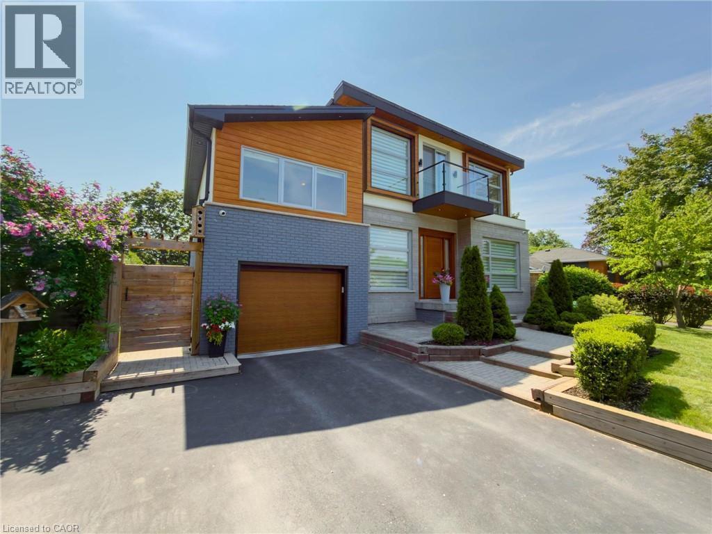 Modern exterior with a wood-finish garage door, grey brick and wood-finish siding, a second-story balcony with glass railing, a paved driveway, and established front landscaping - 5178 Hunter Drive, Burlington, ON - Outdoor