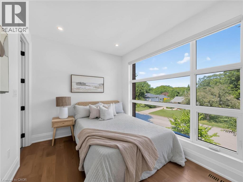 Expansive window wall with multiple panes, hardwood-finish flooring, recessed lighting, and crisp white walls - 5178 Hunter Drive, Burlington, ON - Indoor Photo Showing Bedroom