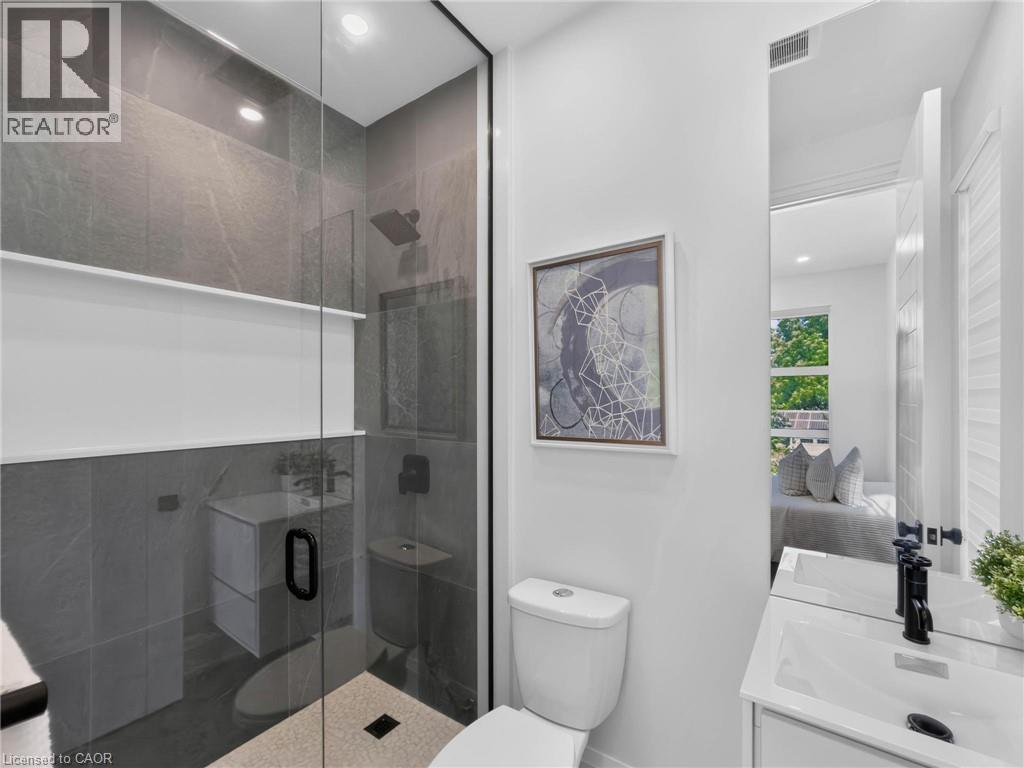 Modern bathroom featuring a glass-enclosed shower with dark tile surround, a built-in shower shelf, a white vanity with an integrated sink, and a toilet - 5178 Hunter Drive, Burlington, ON - Indoor Photo Showing Bathroom