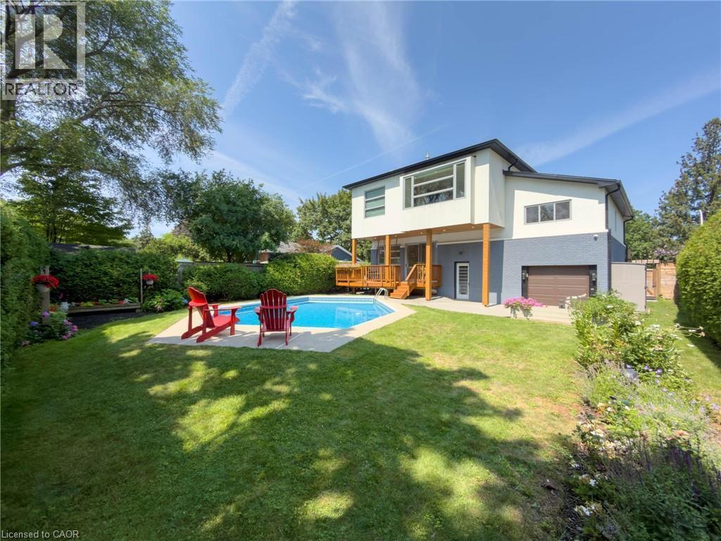 Spacious backyard featuring a large inground swimming pool with surrounding concrete patio, expansive lawn, mature perimeter landscaping, and a multi-level wood deck - 5178 Hunter Drive, Burlington, ON - Outdoor With In Ground Pool