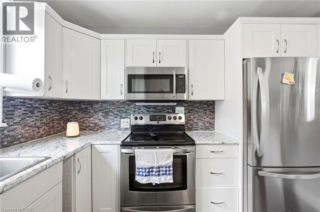 Modern kitchen featuring white shaker-style cabinetry, granite countertops, and a mosaic tile backsplash - 127 Taylor Avenue, Hamilton, ON - Indoor Photo Showing Kitchen With Upgraded Kitchen