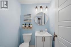 Powder room featuring a white single-sink vanity with cabinet storage, a circular beaded mirror, and a three-light vanity fixture with clear glass shades - 