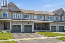 Gray siding exterior featuring multiple dormer windows, a covered front porch, and an attached two-car garage with green sectional doors - 
