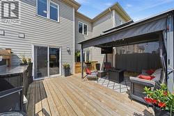 Expansive wooden deck featuring a covered gazebo area with string lighting, a built-in outdoor kitchen with a dark countertop, and direct access through a sliding glass door - 