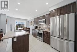 Kitchen featuring dark wood cabinetry, stainless steel appliances, a tiled backsplash, and light-toned countertops - 