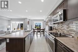 Open-concept kitchen featuring an island with a double basin sink, stainless steel appliances, dark wood cabinetry, and a mosaic tile backsplash - 