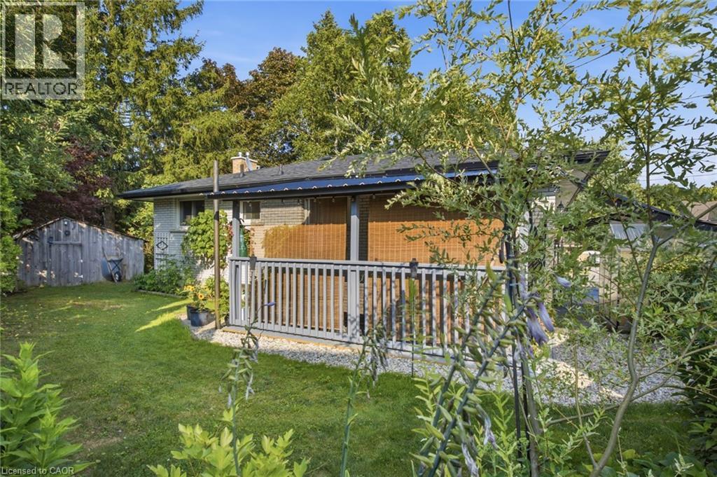 Rear exterior featuring a covered porch with a slatted railing, a manicured lawn, and mature trees - 11 Summit Crescent, Guelph, ON - Outdoor With Deck Patio Veranda
