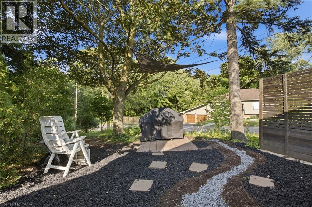 Landscaped outdoor area featuring black and grey gravel, a privacy fence, and mature trees - 11 Summit Crescent, Guelph, ON - Outdoor