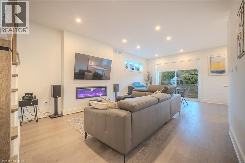 Spacious living area featuring light wood-finish flooring, recessed lighting, an electric fireplace with color-changing flame effect, and a large sliding glass door opening to an outdoor patio - 9 Princeton Common, St. Catharines, ON - Indoor Photo Showing Living Room With Fireplace