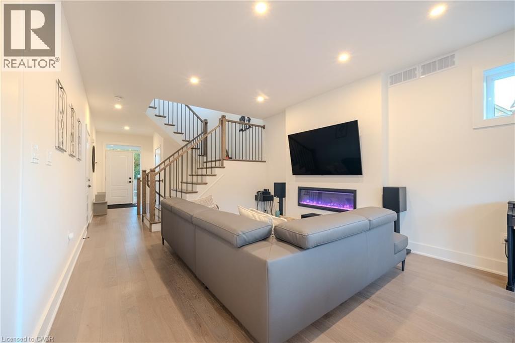 Open-concept living area featuring light wood-finish flooring, recessed lighting, a modern electric fireplace, and a contemporary staircase with wood treads and metal balusters - 9 Princeton Common, St. Catharines, ON - Indoor With Fireplace