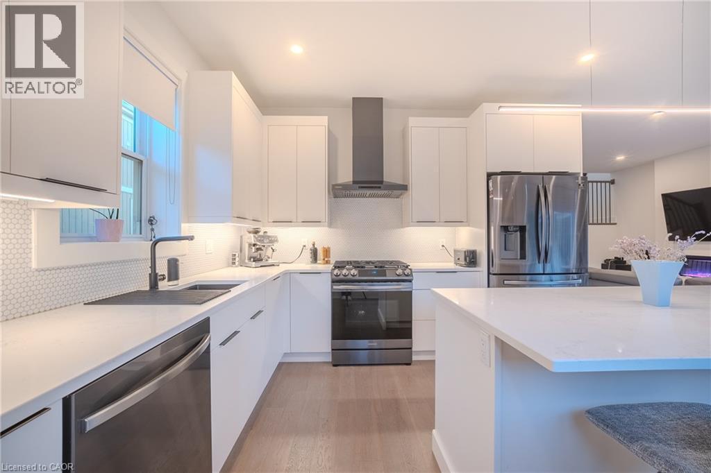 Modern kitchen featuring white flat-panel cabinetry, light-toned countertops, a stainless steel gas range with coordinating vent hood, and a deep undermount sink with a matte black faucet - 9 Princeton Common, St. Catharines, ON - Indoor Photo Showing Kitchen With Stainless Steel Kitchen With Upgraded Kitchen