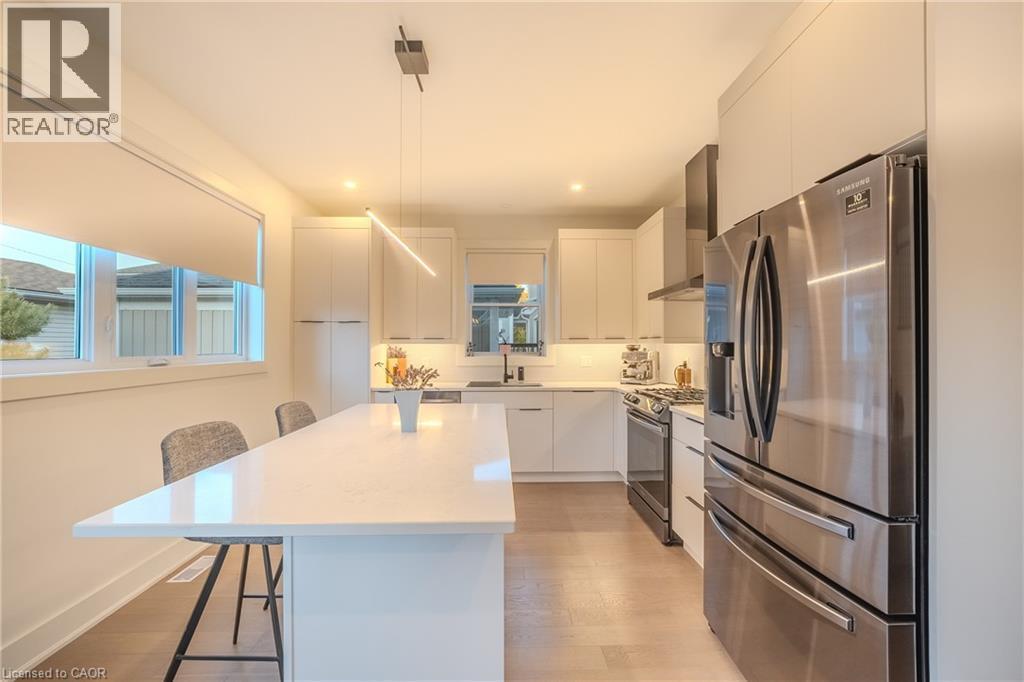 Modern kitchen featuring a large island with seating, stainless steel appliances, white cabinetry, and wood-finish flooring - 9 Princeton Common, St. Catharines, ON - Indoor Photo Showing Kitchen With Stainless Steel Kitchen