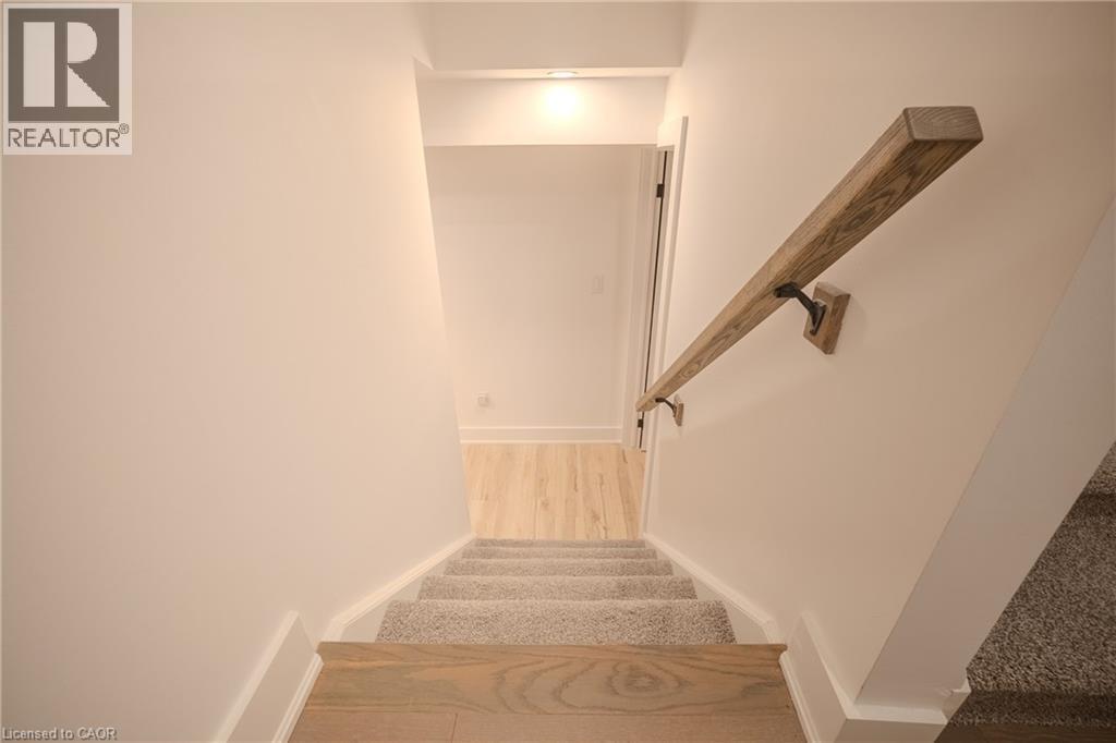 Staircase featuring wood-finish treads and risers, carpeted steps, a wood-finish handrail with black iron brackets, and white wall finishes - 9 Princeton Common, St. Catharines, ON - Indoor Photo Showing Other Room