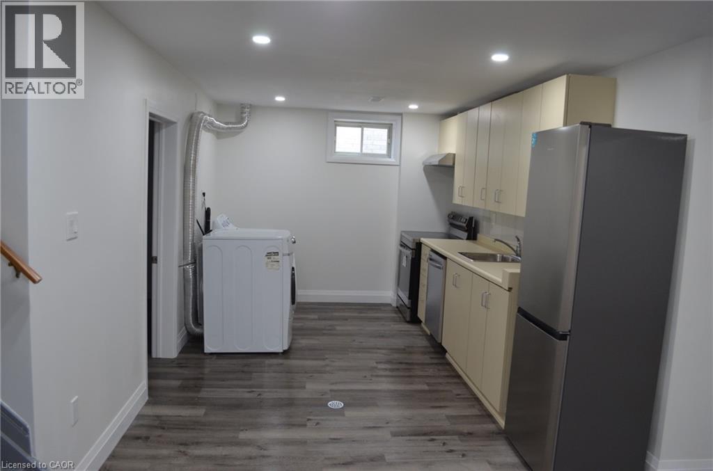 Compact kitchen area featuring wood-finish flooring, recessed lighting, and a stainless steel refrigerator - 275 Locheed Drive Unit# Lower, Hamilton, ON - Indoor Photo Showing Laundry Room