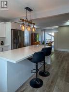 Spacious kitchen featuring a waterfall-edge island with seating, white cabinetry, stainless steel refrigerator, and wood-finish flooring - 