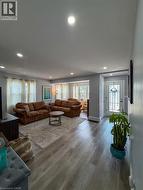 Bright living area featuring recessed ceiling lighting, wood-finish flooring, and multiple windows with curtain rods - 