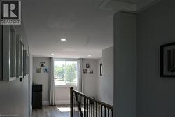Upper-level landing featuring wood-finish flooring, a white trim window, recessed lighting, and a dark wood-finish railing - 