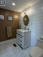 Bathroom featuring white shiplap accent wall, white tile flooring, and a single-sink vanity with a sliding barn door cabinet - 