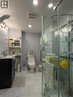 Basement bathroom featuring a glass-enclosed shower, rectangular white floor tiles, a dark vanity with a single sink, an integrated toilet, and recessed lighting - 