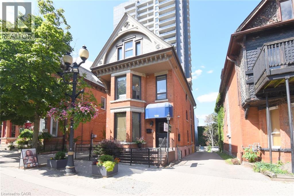 Brick exterior with a prominent bay window, arched gable dormer, and a blue awning - 108 George Street, Hamilton, ON