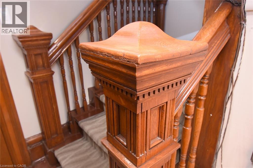 Ornate wood-finish newel post with detailed carvings and decorative trim, accompanied by a matching wood-finish handrail and balusters, framing a carpeted staircase - 108 George Street, Hamilton, ON