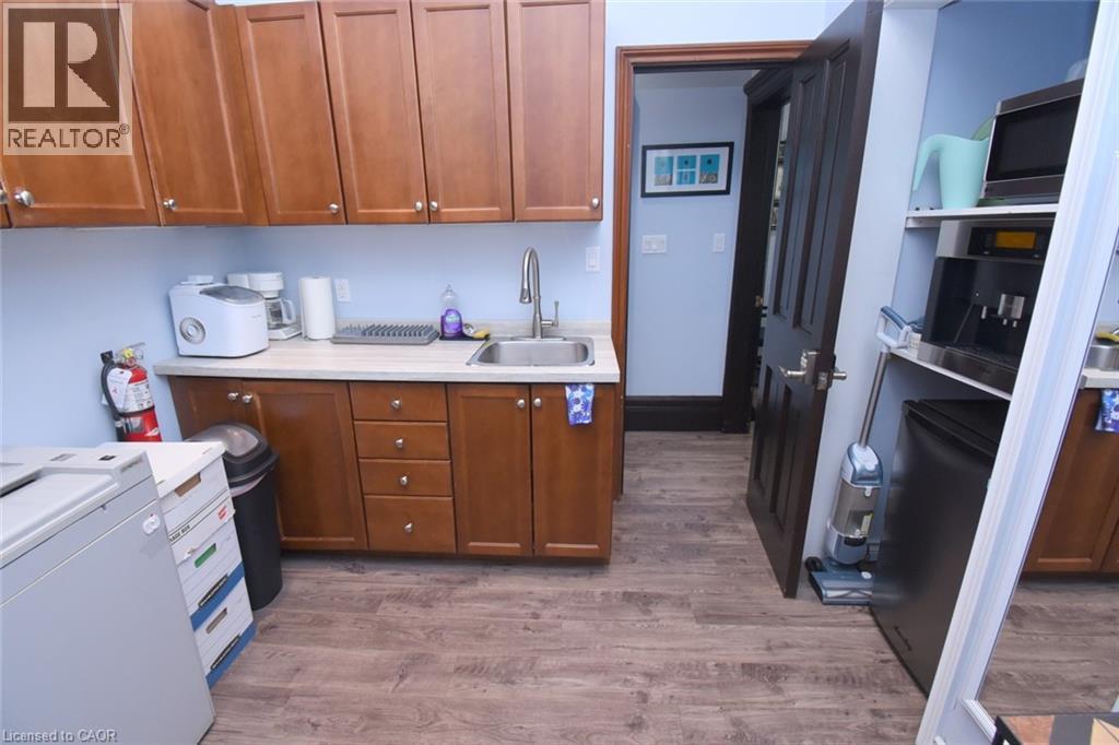 Functional kitchen area featuring wood-finish flooring, light blue walls, and amber-toned cabinetry with silver hardware - 108 George Street, Hamilton, ON