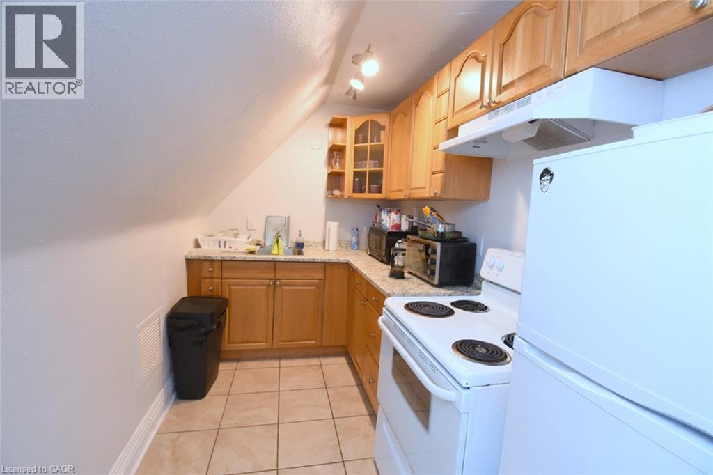 Compact kitchen featuring wood cabinetry, solid surface countertops, a white electric range, and a white refrigerator - 108 George Street, Hamilton, ON