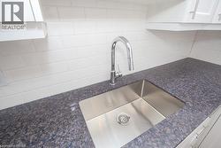 Kitchen featuring a stainless steel undermount sink with a high-arch chrome faucet, speckled dark countertop, and a white subway tile backsplash - 