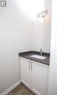 Bathroom vanity featuring a dark stone countertop, white cabinetry with brushed nickel hardware, an undermount sink, and a chrome faucet - 